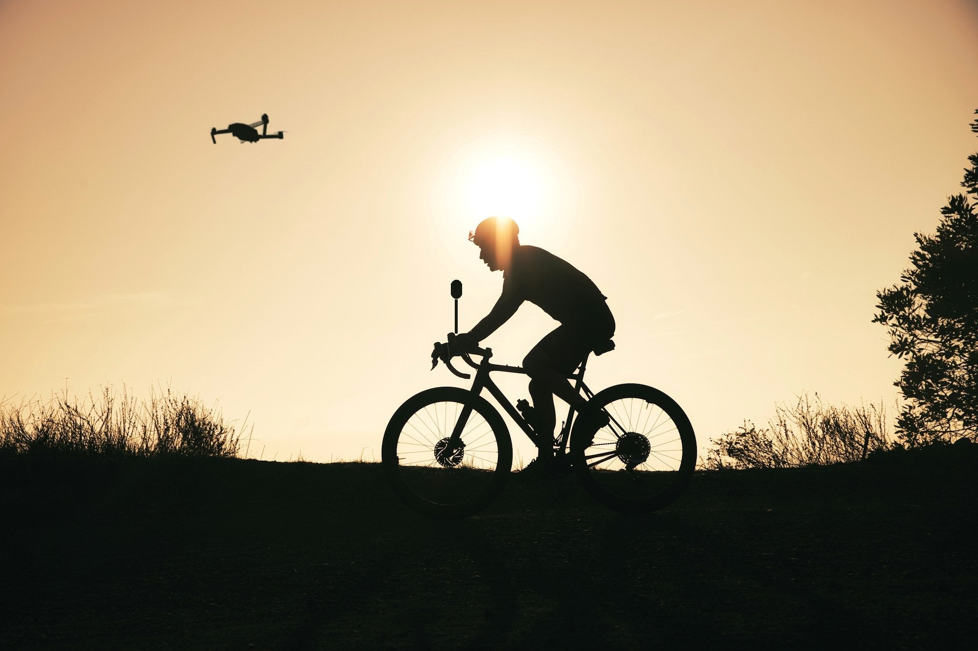 Cycliste en silhouette au sommet d'une colline au coucher du soleil, caméra 360 sur le vélo et drone dans le ciel